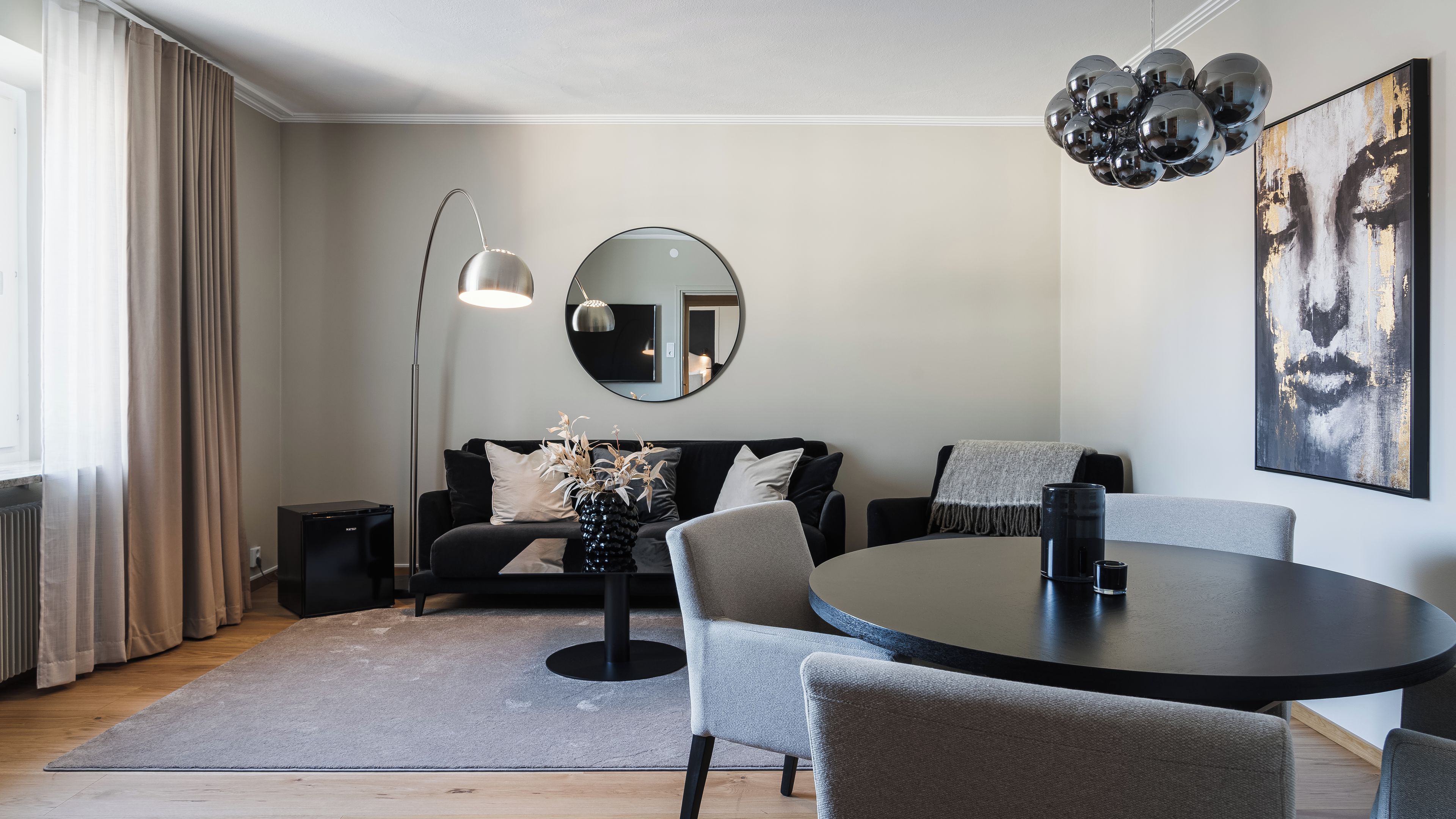 A modern living room with a round dining table, a sofa, a floor lamp, and a large mirror on the wall.