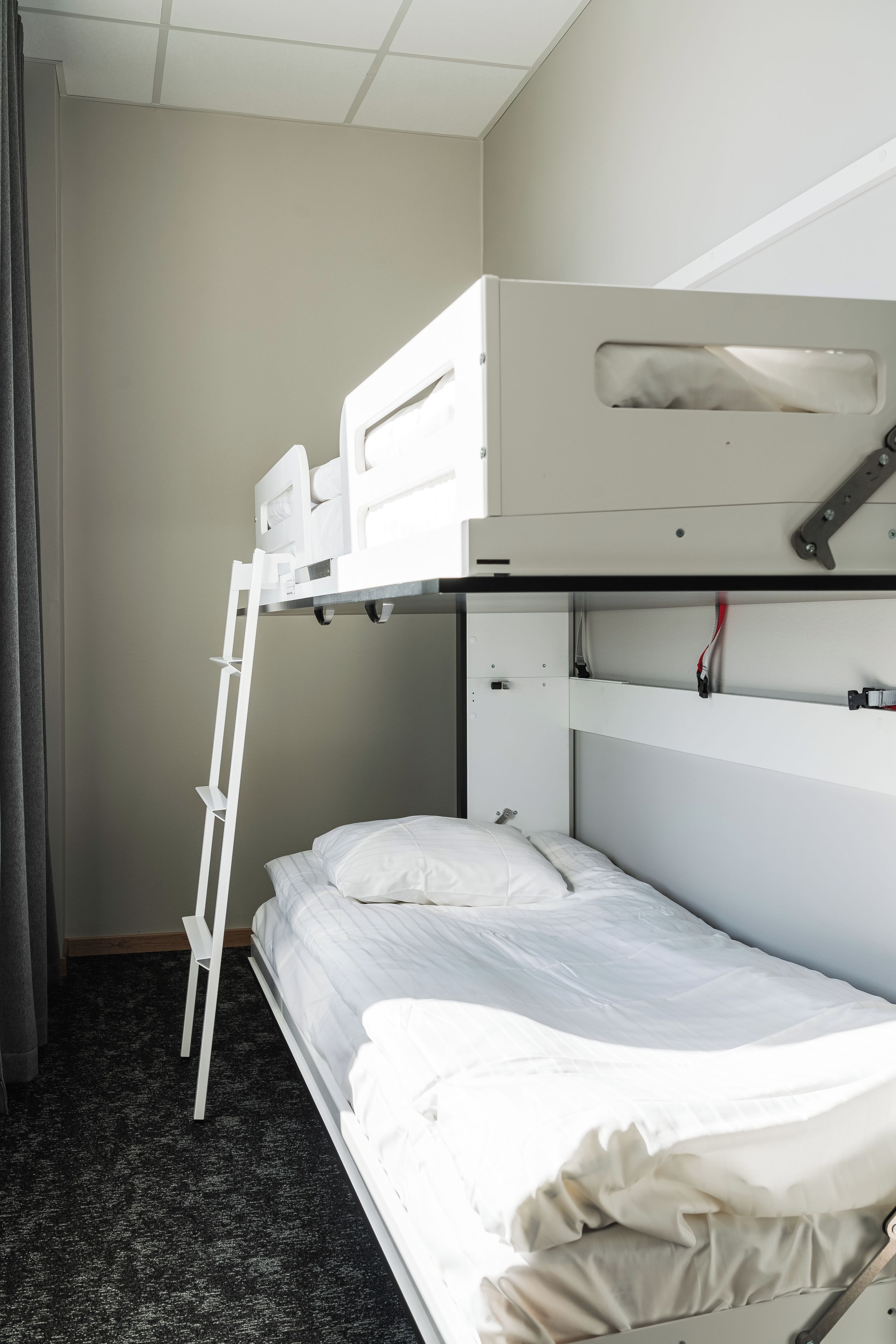 Una cama litera con escalera, una cama individual abajo y un pequeño espacio de almacenamiento en la cama superior.