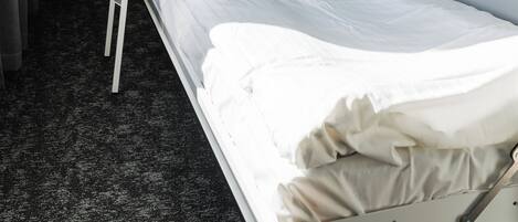 Una cama litera con escalera, una cama individual abajo y un pequeño espacio de almacenamiento en la cama superior.