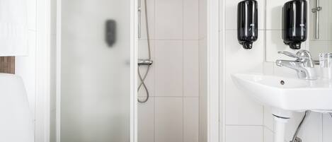 Un baño moderno con un lavabo blanco, dos dispensadores de jabón negros, un grifo cromado y una ducha con puerta de cristal.