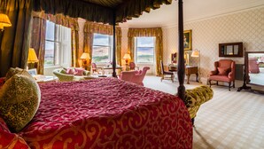 A spacious bedroom with a large bed, multiple seating areas, and a view of the outdoors through large windows. - Inverlochy Castle (Fort William)