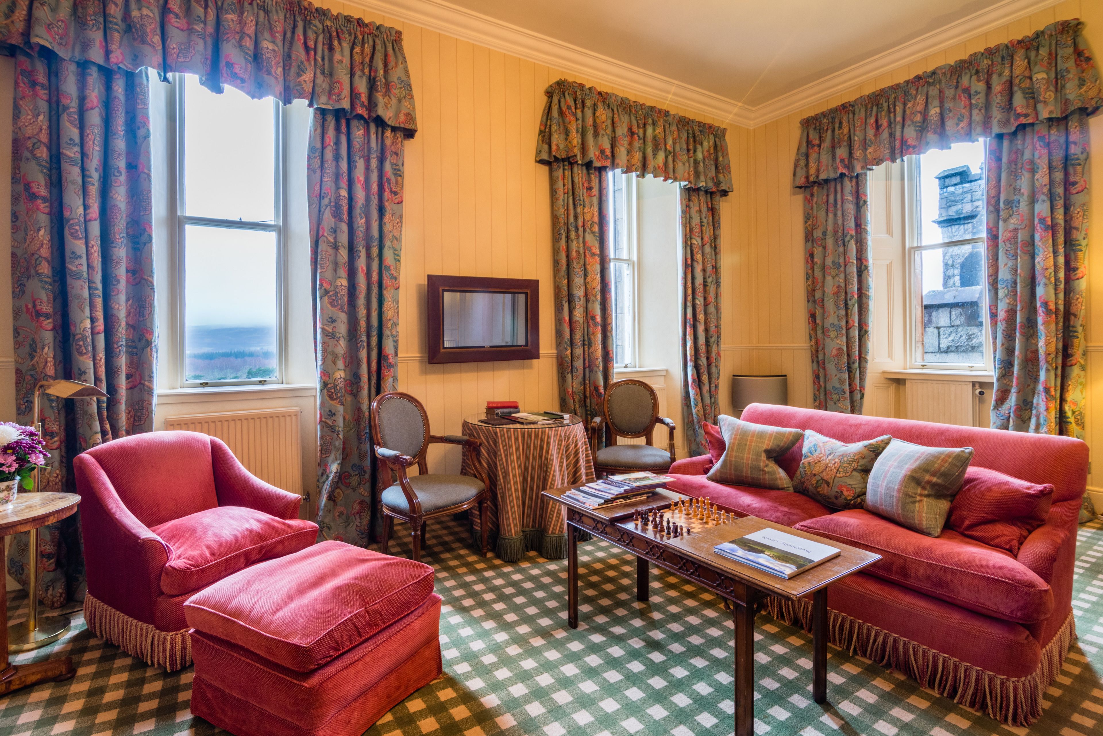A cozy living room with a checkered floor, a red sofa, a wooden coffee table, and a chessboard.