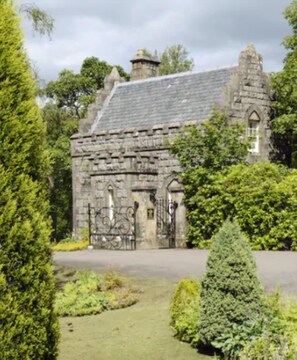 A historic stone building with a traditional design, surrounded by lush greenery and a well-maintained garden.