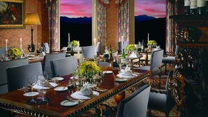A formal dining room with a long table set for a meal, two large windows with curtains, and a wine rack on the right. - Inverlochy Castle (Fort William)