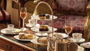 A three-tiered tea service set on a table with a floral-patterned chair in the background.