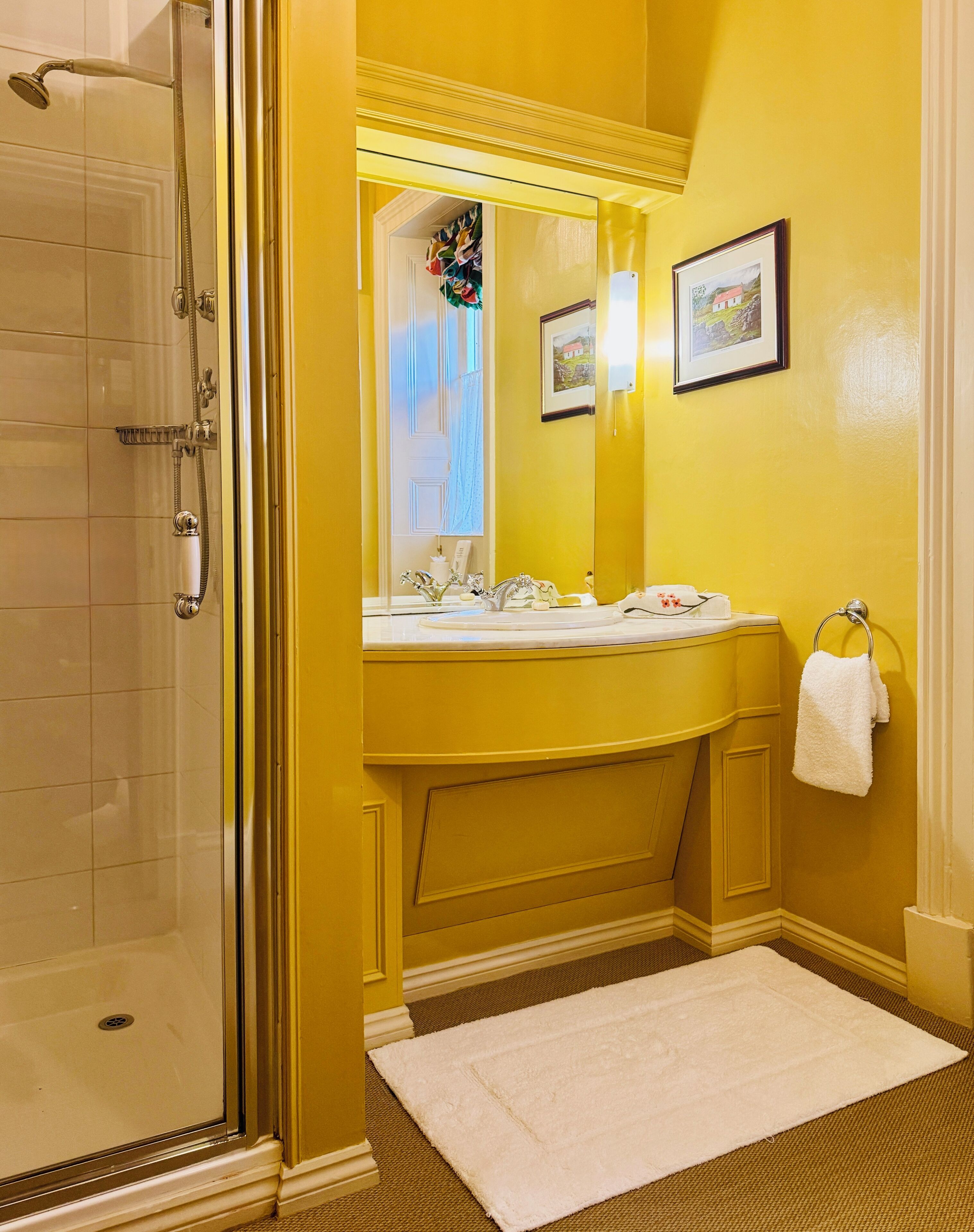 A bathroom with a glass shower enclosure, a double sink vanity, a white towel hanging on a towel rack, and a framed picture on the wall.