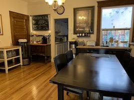 A modern kitchen with a wooden table, chairs, a coffee machine, and a chalkboard menu.