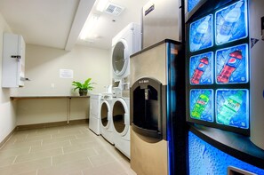 Un espace buanderie équipé d’un lave-linge, d’un sèche-linge et d’un distributeur d’eau affichant des publicités pour des boissons.