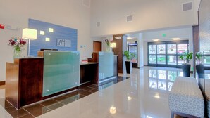 A modern reception area with a glass partition, a reception desk, a blue wall with a clock, and a seating area with a patterned bench. - Holiday Inn Express & Suites Carlsbad Beach by IHG (Carlsbad)