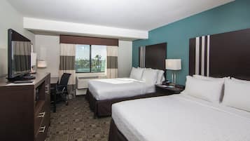 A hotel room with two beds, a desk, a chair, a TV, and a window with curtains.