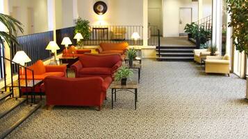 A lobby with a staircase, red sofas, and potted plants.