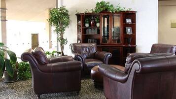 A lobby with leather chairs, a wooden cabinet, and potted plants.