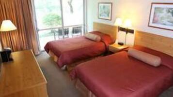 A hotel room with two beds, a wooden nightstand, a lamp, and a window with curtains.