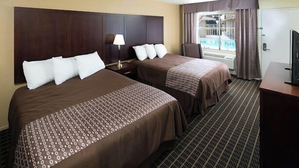 A hotel room with two beds, a TV, a desk, and a view of a pool. - GuestPlace Inn & Suites (Redding)
