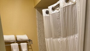 A bathroom with a toilet, a bathtub, and a shower curtain. There are towels hanging on a rack. - GuestPlace Inn & Suites (Redding)