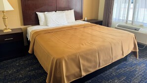 A hotel room with a large bed, a wooden headboard, a bedside table with a lamp, and an air conditioning unit. - GuestPlace Inn & Suites (Redding)