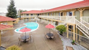 A motel with a swimming pool, outdoor seating, and a red-roofed building. - GuestPlace Inn & Suites (Redding)