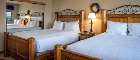 Habitación de hotel con dos camas de madera, una mesita de noche con lámpara y un espejo que refleja la habitación.