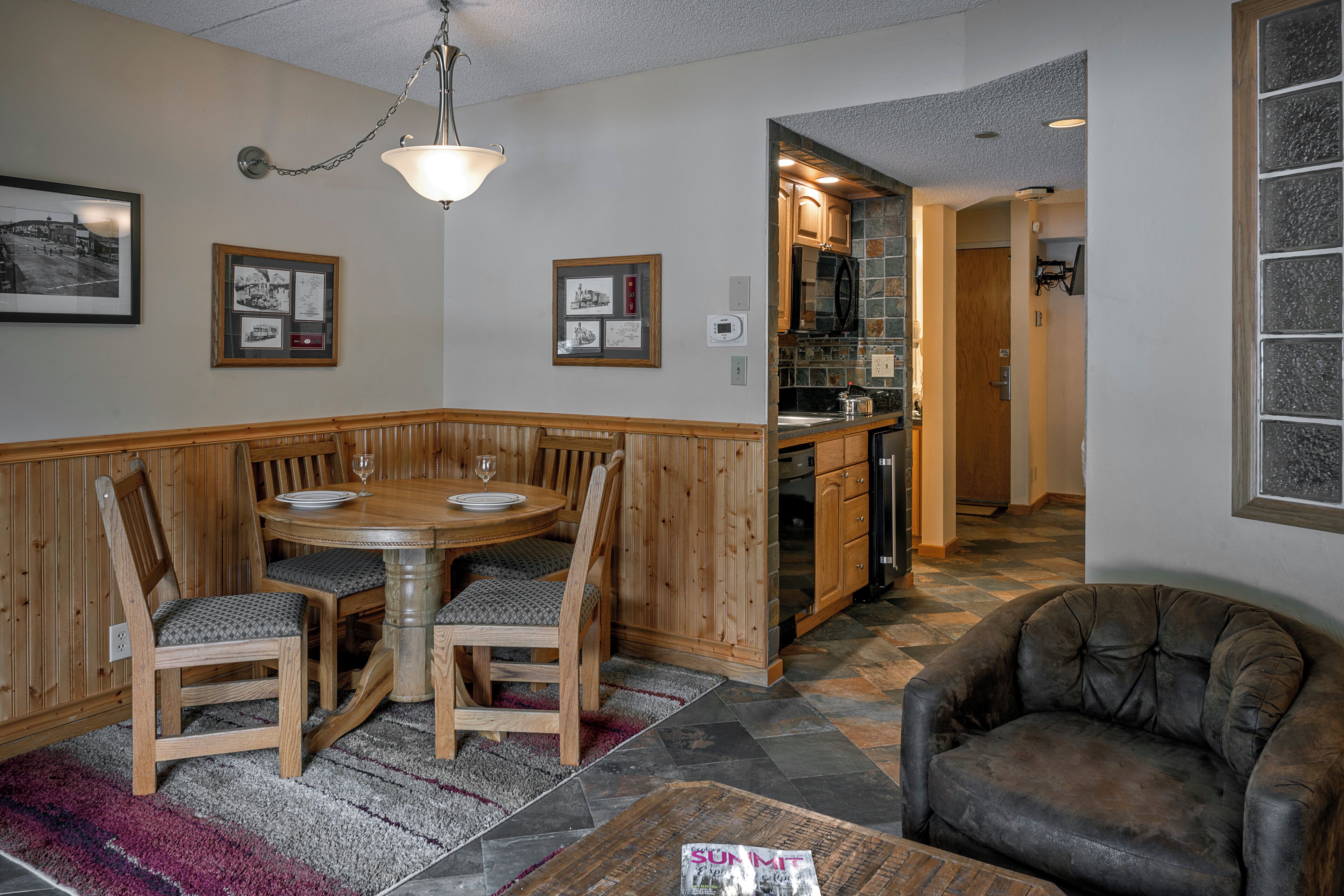 A dining area with a wooden table and chairs, a leather sofa, and a kitchen in the background.