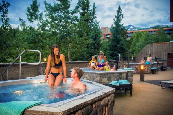 A hot tub area with stone walls and a view of trees and buildings in the background.