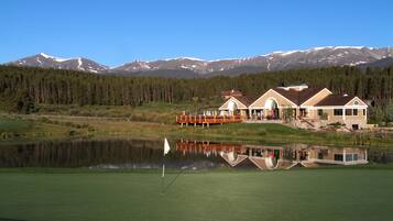 Enjoy a serene golf experience with a picturesque backdrop of snow-capped mountains and a tranquil pond.