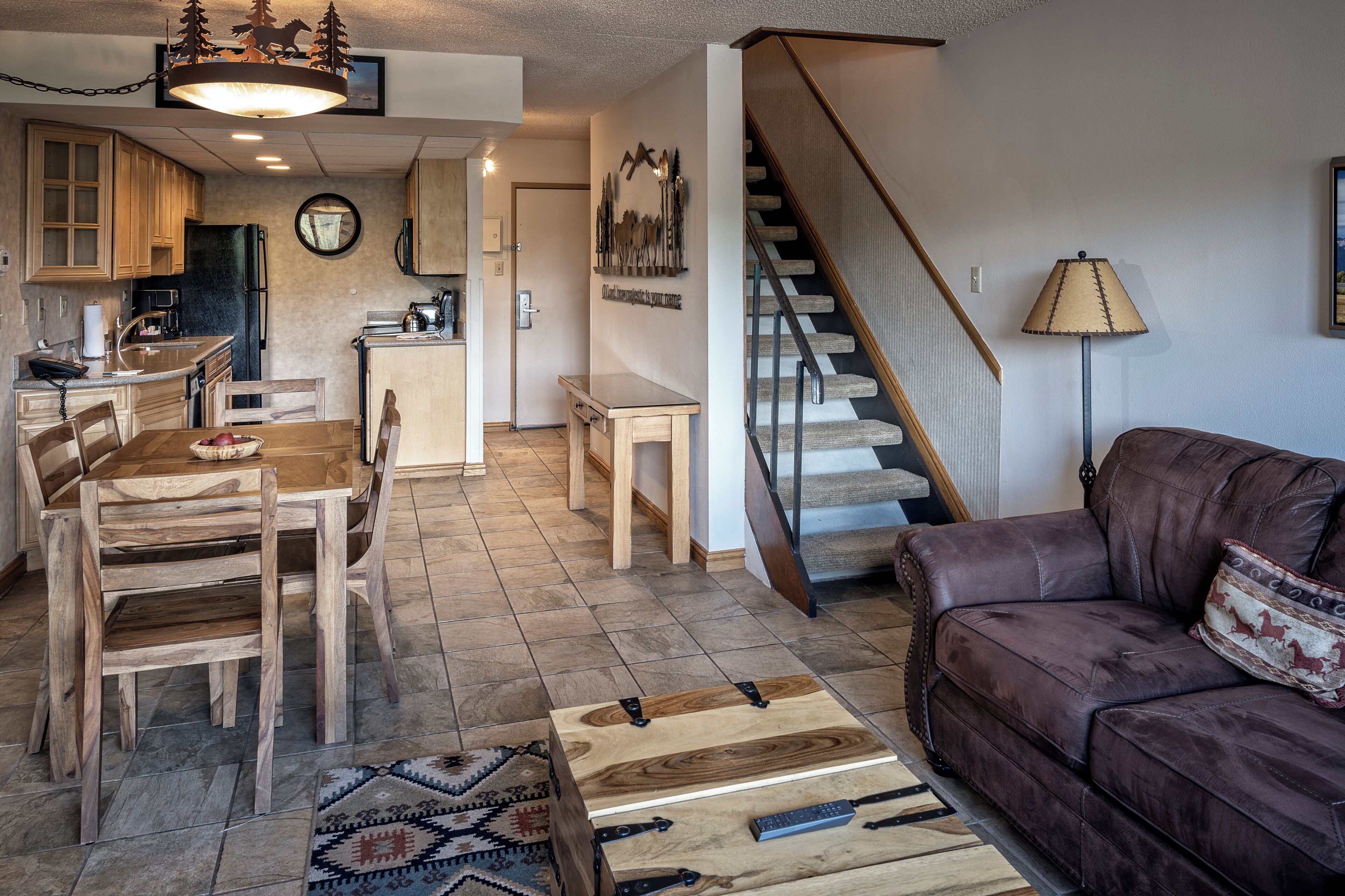 A spacious living area with a wooden dining table, leather sofa, and a staircase leading to another level.