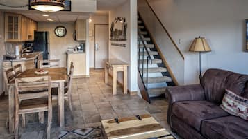 A spacious living area with a wooden dining table, leather sofa, and a staircase leading to another level.