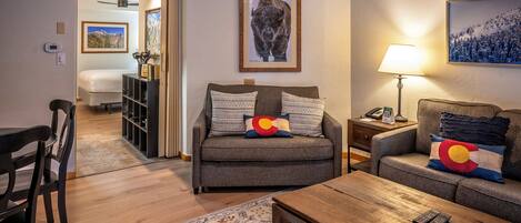 A living room with a sofa, a coffee table, and a TV. There is a lamp on a side table.