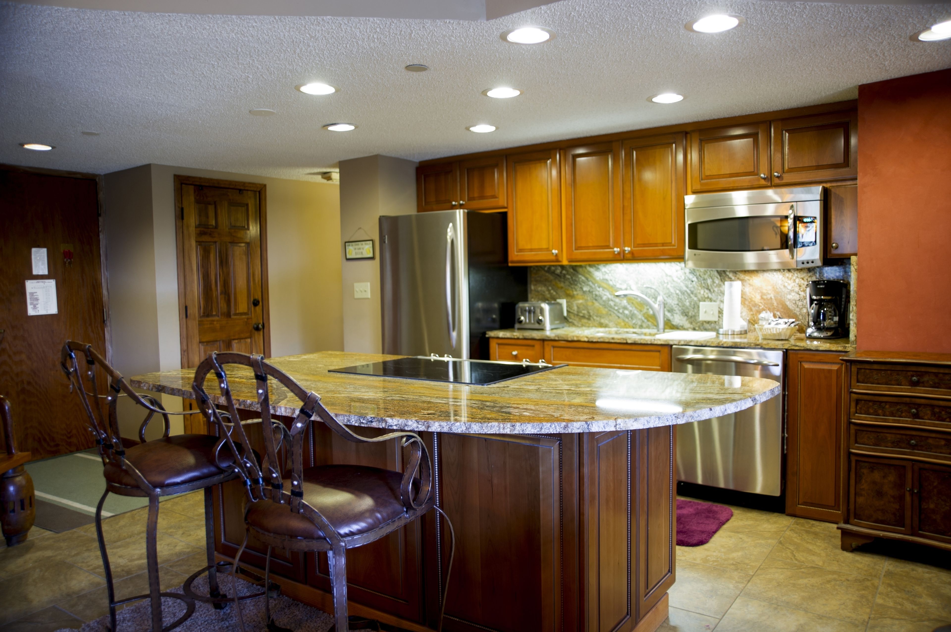 A kitchen with wooden cabinets, stainless steel appliances, and a granite countertop island with bar stools.
