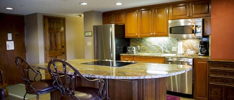 A kitchen with wooden cabinets, stainless steel appliances, and a granite countertop island with bar stools.