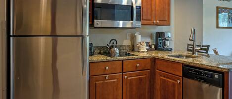 A kitchen with wooden cabinets, stainless steel appliances, granite countertops, and a coffee maker.