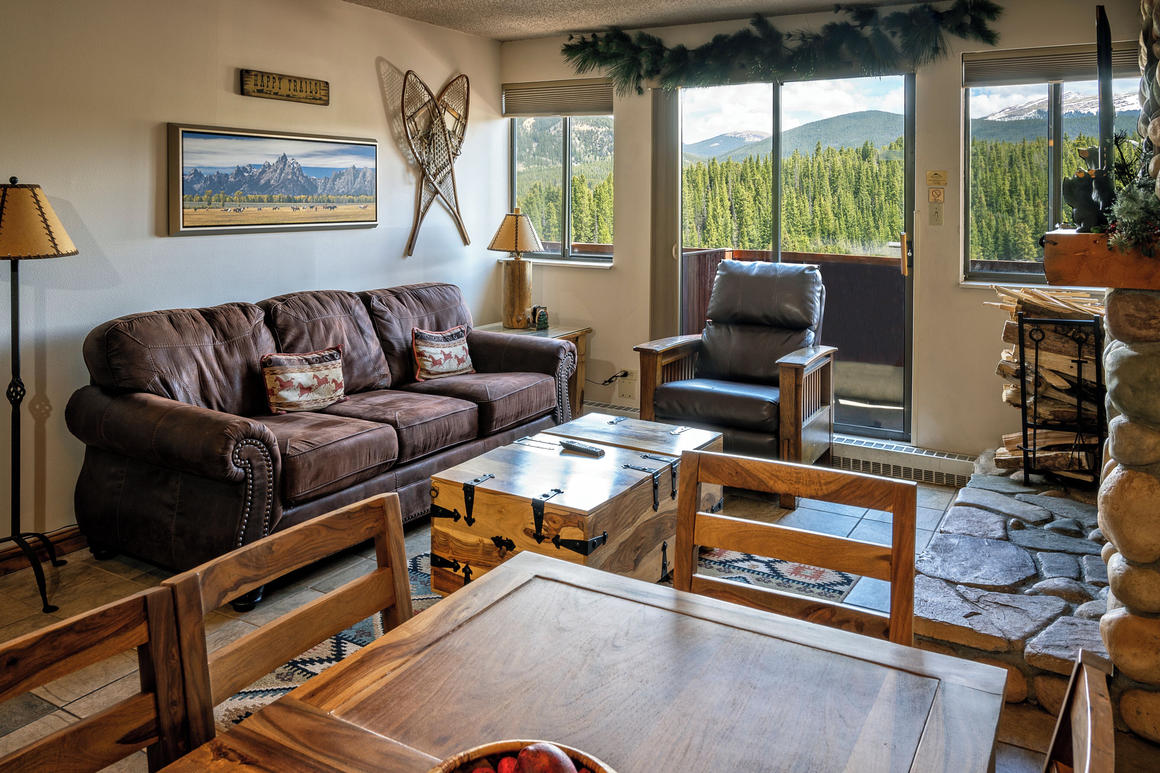 A cozy living room with a brown leather couch, a wooden coffee table, and a stone fireplace.