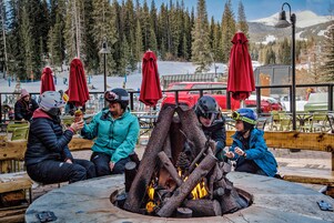 Un grupo de personas sentadas alrededor de una fogata al aire libre, con una montaña nevada de fondo.