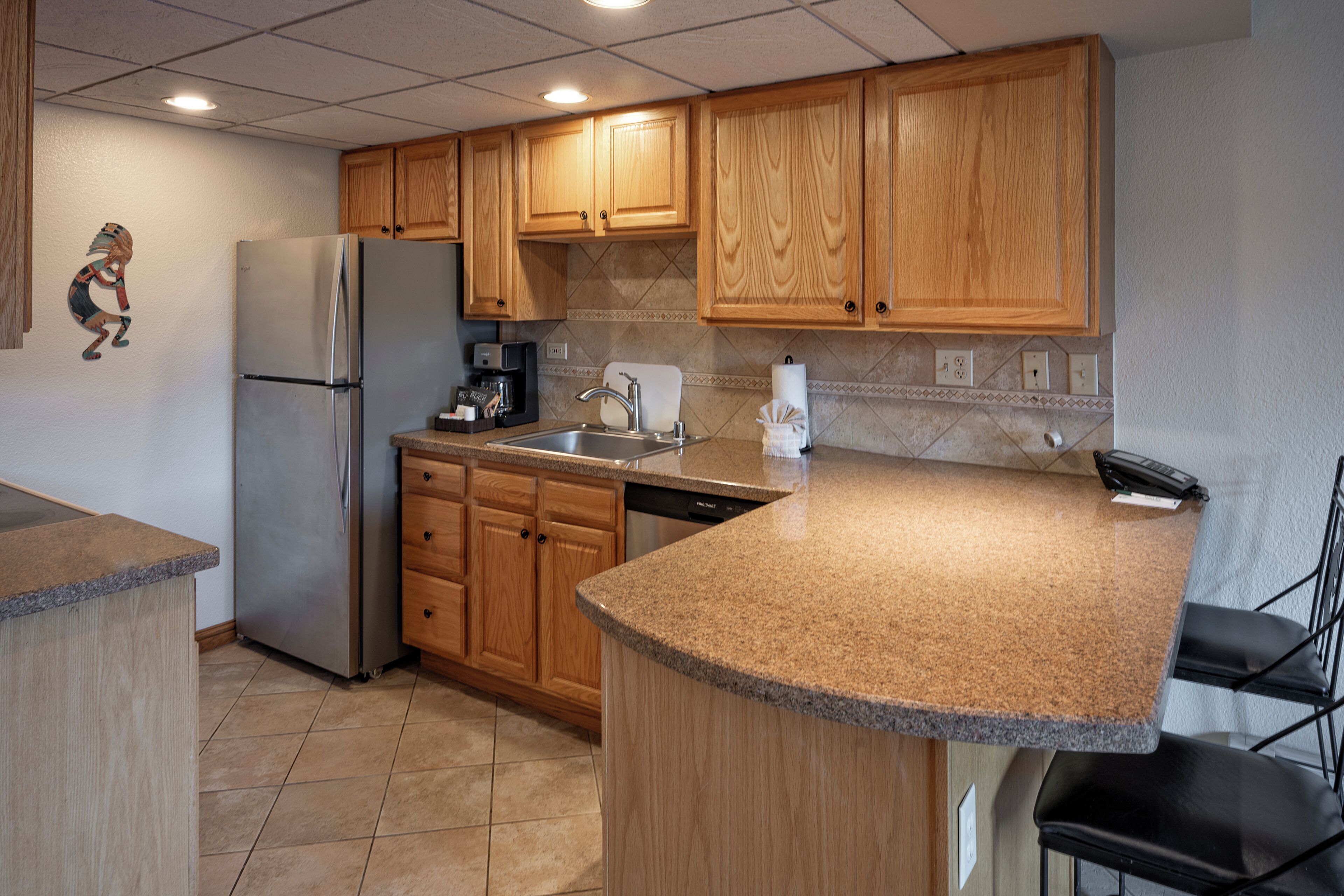 A kitchen with wooden cabinets, a stainless steel refrigerator, a dishwasher, a granite countertop, and a sink.