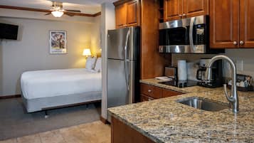A compact hotel room with a bed, kitchenette, and a ceiling fan.