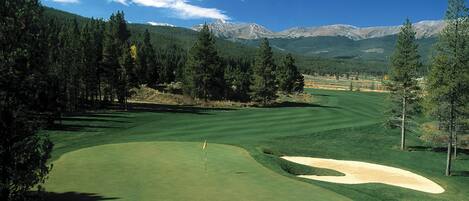 A golf course with a flagstick, sand bunkers, and a mountainous backdrop.