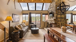 A spacious living area with a stone fireplace, a wooden ceiling, and large windows offering a view of the outdoors. - Beaver Run Resort & Conference Center (Breckenridge)