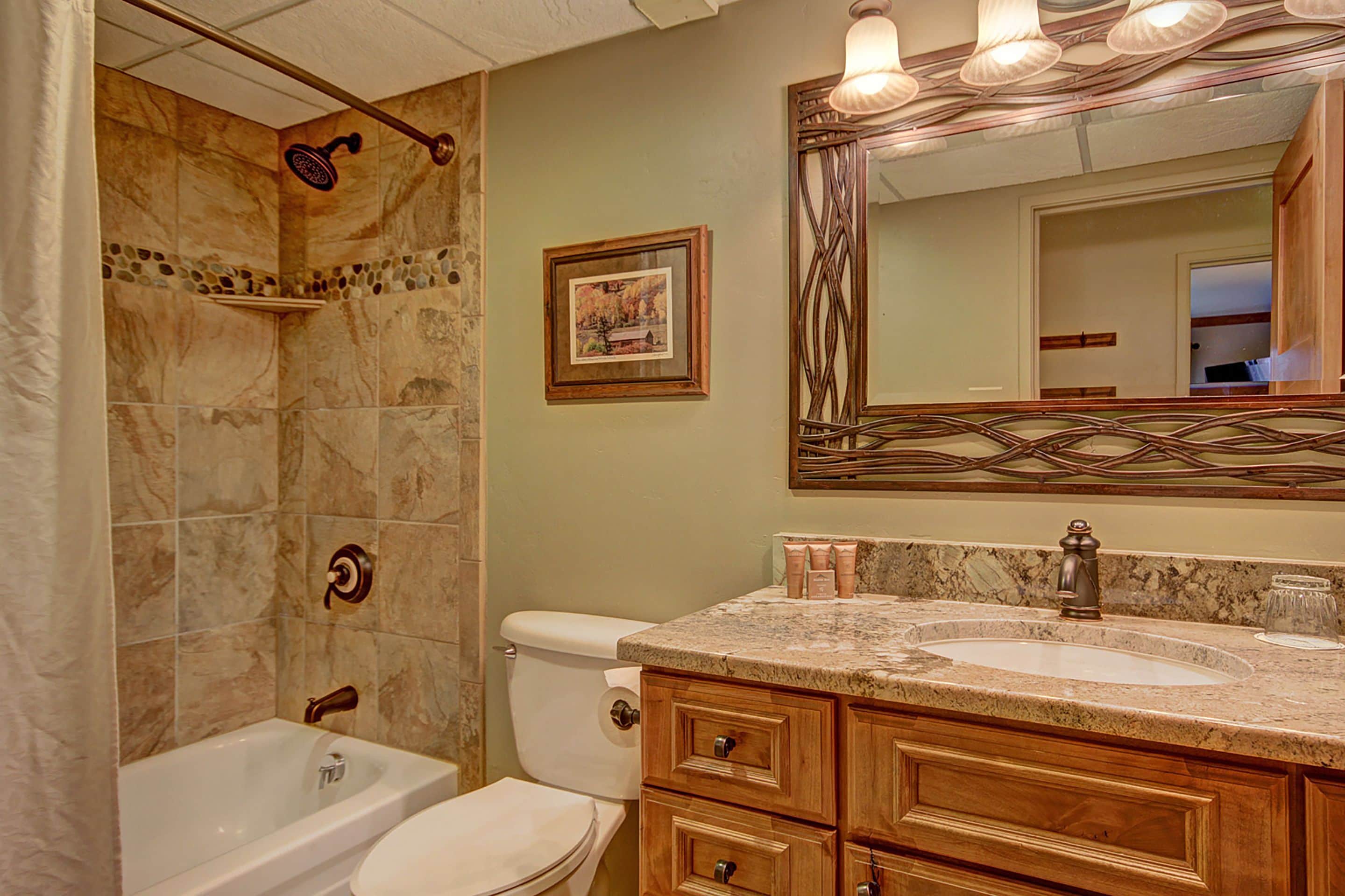 A bathroom with a bathtub, toilet, vanity with a sink, and a mirror.