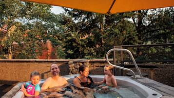 A hot tub with a stone wall and metal railing, surrounded by trees and a stone pathway.