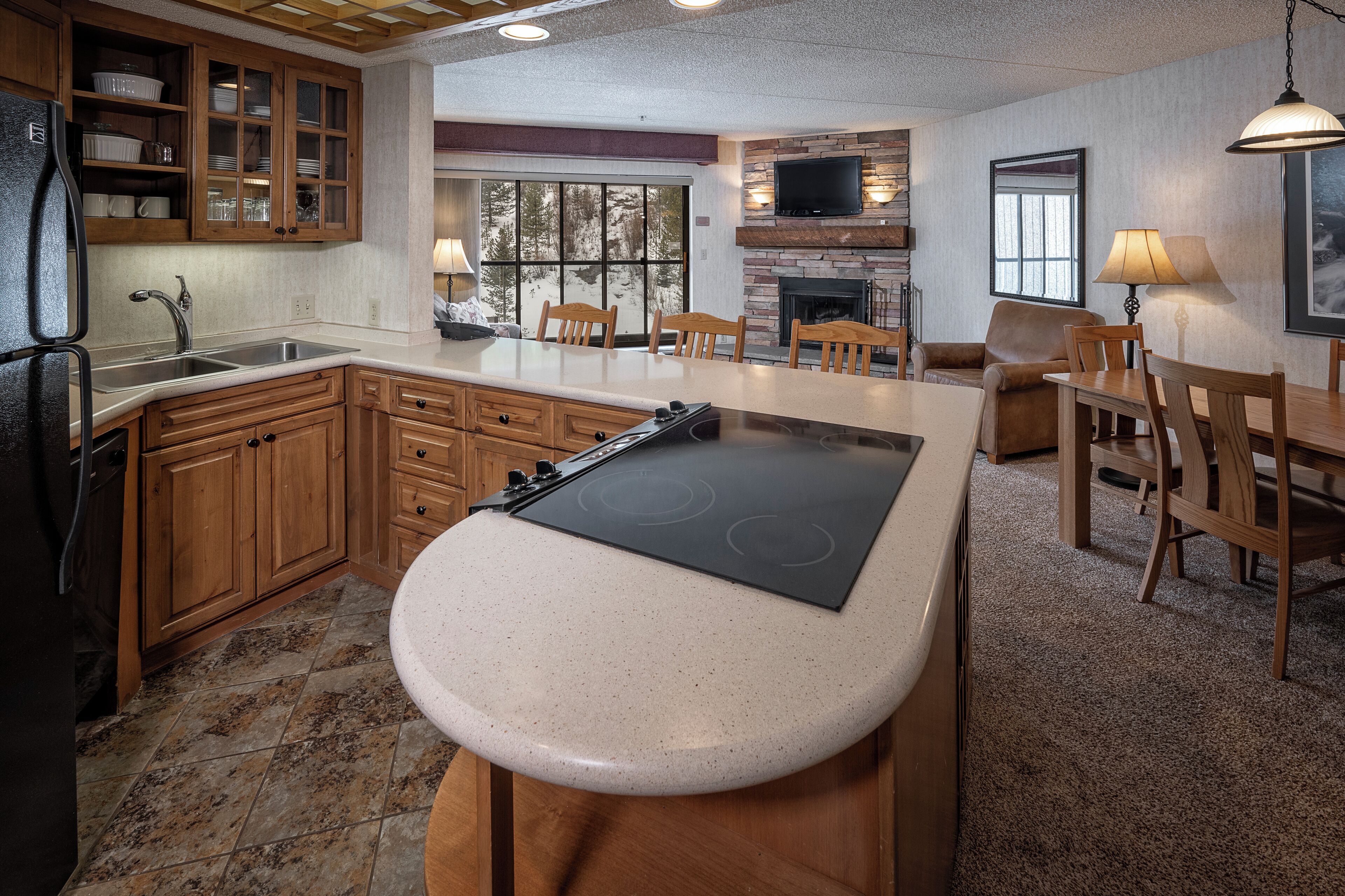 A kitchen with wooden cabinets, a built-in stove, a dining area with a table and chairs, and a fireplace.