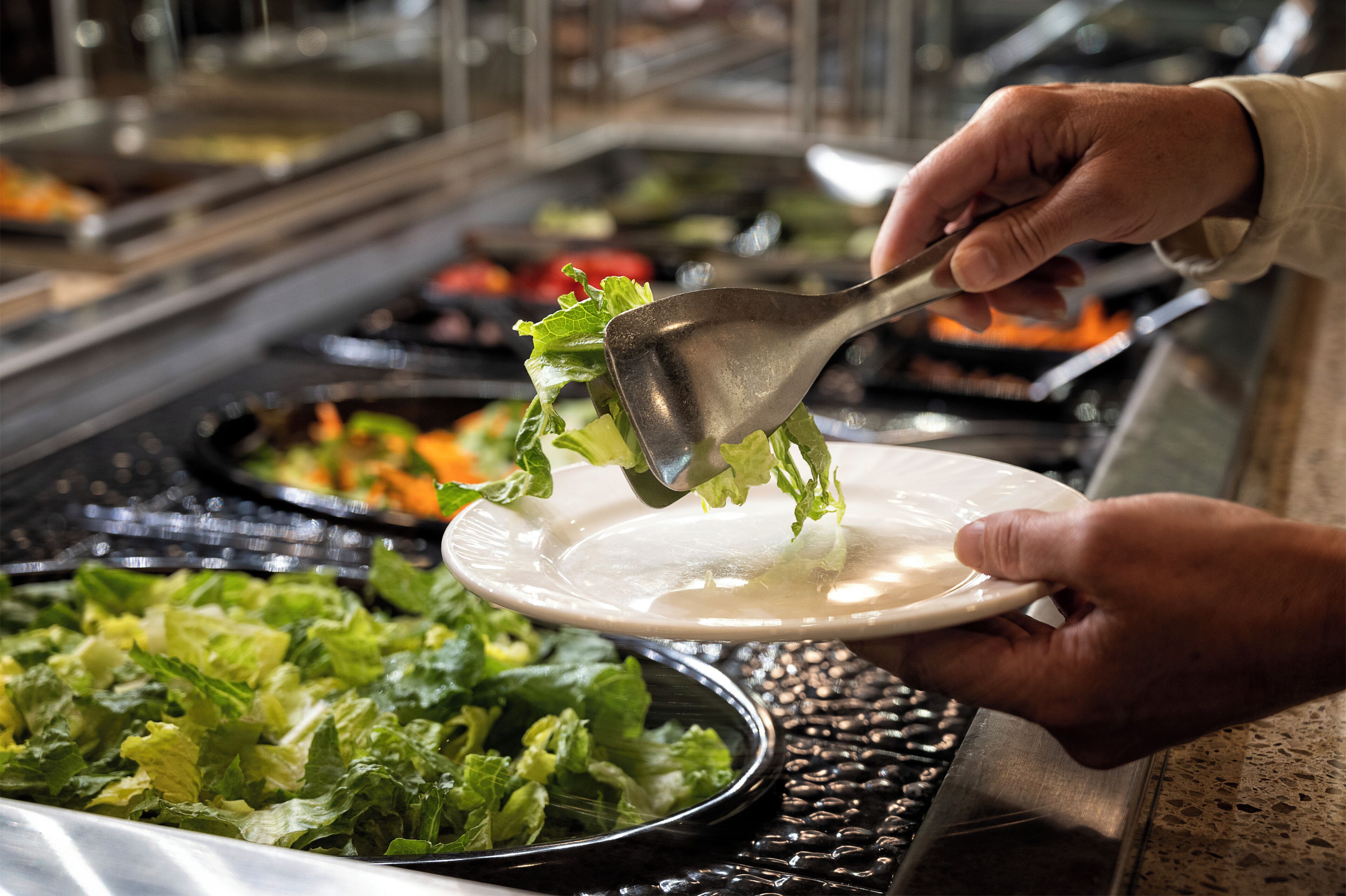 A buffet with various food items, including a plate of salad being served.