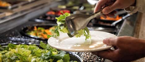 Un bufé con diferentes opciones de comida, incluyendo una bandeja de ensalada siendo servida.