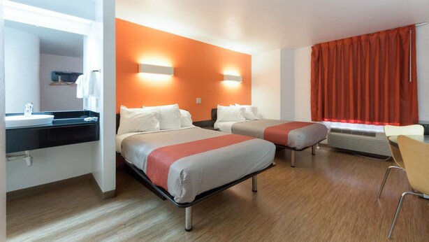 A hotel room with two beds, a bathroom with a sink, and a chair. - Motel 6 Dallas, TX - Northeast (Dallas)
