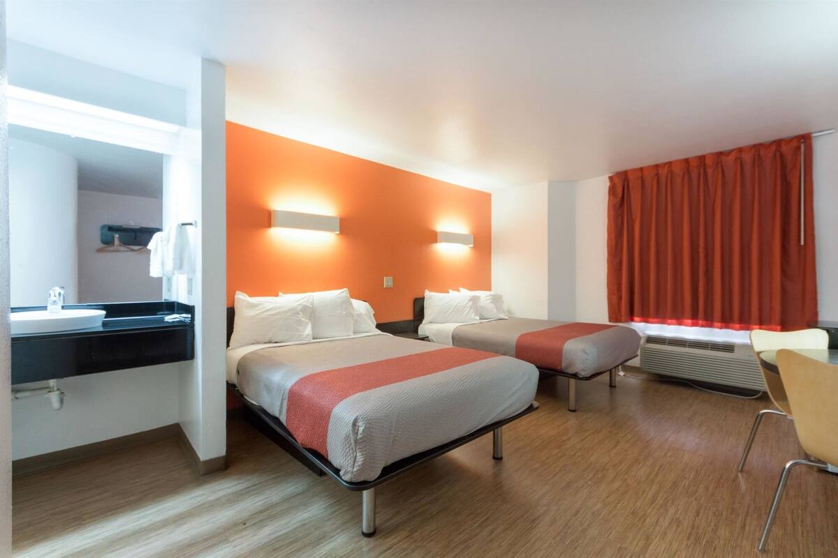 A hotel room with two beds, a bathroom with a sink, and a chair.