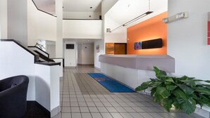 A hotel reception area with a modern design, including a reception desk, a staircase, and a reception wall with a sign. - Motel 6 Dallas, TX - Northeast (Dallas)
