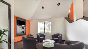 A modern room with a flat-screen TV mounted on the wall, two armchairs, a small round table, and a large window providing natural light. - Motel 6 Dallas, TX - Northeast (Dallas)