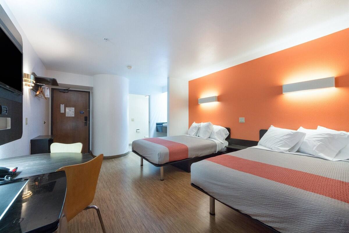 A hotel room with two beds, a desk, and a chair.
