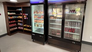 Two Norpole branded refrigerators with shelves stocked with beverages and snacks, and a wooden shelf unit with various food items. - SureStay Studio by Best Western Rowland (Rowland)