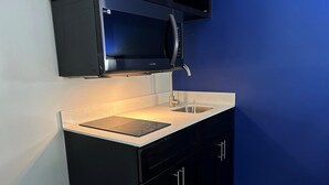 A kitchen with a microwave, sink, and black cabinets. - SureStay Studio by Best Western Rowland (Rowland)