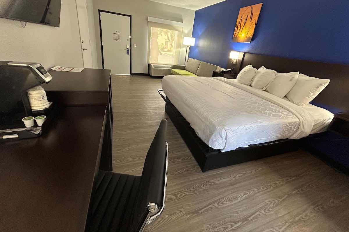 A hotel room with a bed, desk, chair, coffee machine, and a view of the outside.